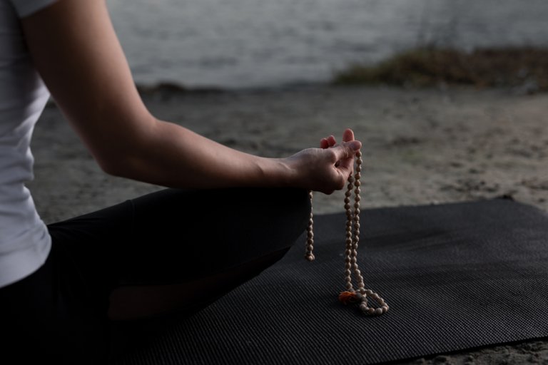 Beautiful young woman is practicing meditation on the river with her mala