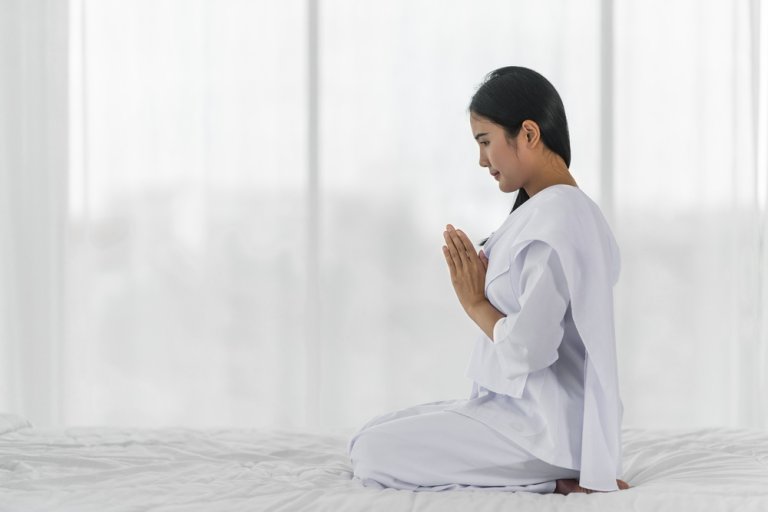 A buddhist woman in white robe praying and chanting with her palms together.